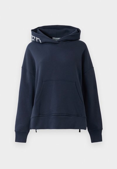 Tumši zils džemperis ar lielu priekšējo kabatu un kapuci, kurā ir balti teksti vienā pusē.