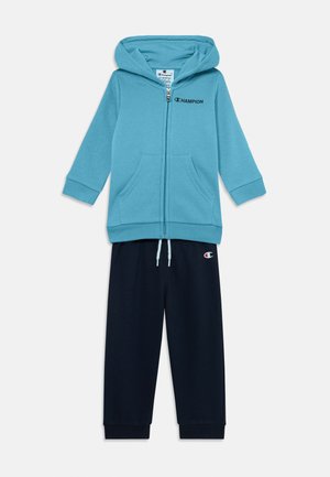 Felpa blu con zip e tasche abbinata a pantaloni tuta blu scuro. Entrambi realizzati in un tessuto morbido, con il logo "Champion" sul petto e sulla gamba dei pantaloni.