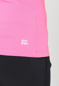 Rosa sporttop med slät textur och en kroppsnära design, med den vita "BIDI BADU"-logotypen nära fållen. Matchad med svarta byxor.