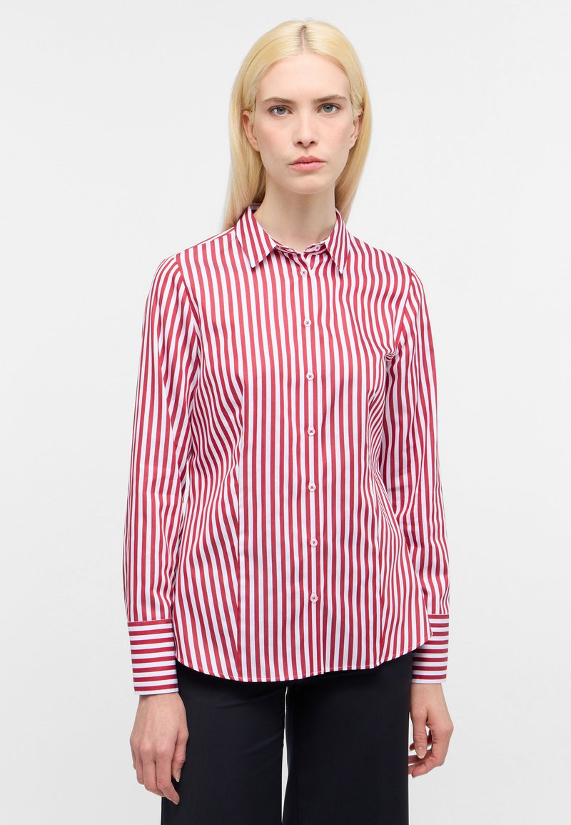 Camicia a righe rossa e bianca con colletto, maniche lunghe e orlo arrotondato; presenta righe verticali alternate e dettagli con bottoni.
