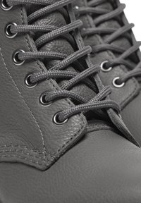 Gros plan sur une botte en cuir gris foncé avec des lacets gris arrondis serrés, passés à travers des œillets en métal.