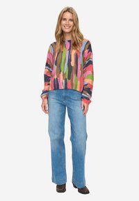 Suéter de punto colorido con una mezcla de patrones en rosa, verde y azul; combinado con jeans de pierna ancha en azul claro y botas marrones.