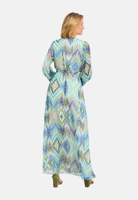 Robe longue et transparente avec un design fluide présentant des motifs de diamants abstraits dans des teintes de vert, bleu et violet. Elle a des manches longues et une taille cintrée.