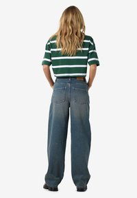 Grønt og hvitt stripete cropped t-skjorte med korte ermer, kombinert med høydejusterte bukser i vidde med blå denim. Teksturert stoff og baklommer synlige.