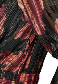 Robe noire avec des motifs à rayures vives rouges, oranges et dorées. Présente un tissu texturé avec des lignes verticales et un détail de fermeture éclair discret.