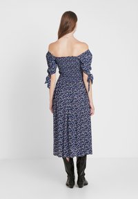 Mönstrad klänning i marinblått med elastisk avskuren halsringning och korta puffärmar. Har en smockad midja och en flödande kjol.