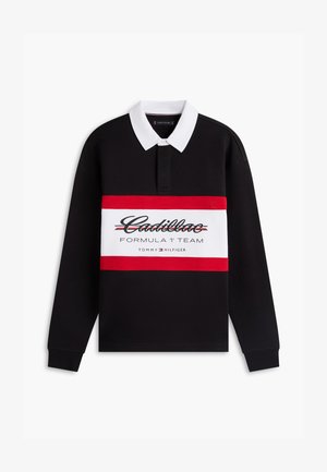 Polo noir à manches longues avec col blanc, bande horizontale rouge et blanche sur la poitrine affichant le texte "Cadillac Formula 1 Team Tommy Hilfiger".