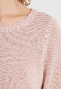 Pullover lavorato a maglia di un delicato rosa chiaro, con scollatura rotonda, caratterizzato da un motivo testurizzato e dettagli a costine nel colletto e nei polsini.