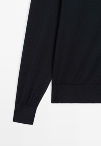 Svart stickad tröja med långa ärmar, ribbade muddar och nederkant. Slät textur med en enkel, klassisk design, utan synliga mönster eller detaljer.