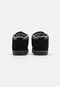 Sapatilhas mid-top pretas em camurça com forro de fleece cinza, bico redondo e sola de borracha texturizada, apresentando um calcanhar reforçado e detalhe do logótipo.