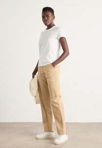 White cotton t-shirt paired with beige cargo pants featuring pockets, and white sneakers. Smooth textures, relaxed fit, casual design.