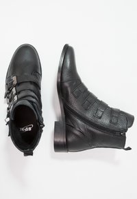 Botines de cuero negro con acabado texturizado, tres correas ajustables con hebillas metálicas y una cremallera lateral. Diseño de tacón plano.