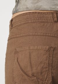 Bruna bomullsshorts med en synlig bakficka, med strukturerad väv och detaljerad sömnad längs midjebandet och fickkanten.