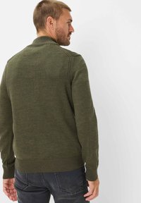 Gestreifter Pullover in Olivgrün mit geripptem Kragen und Bündchen, ausgestattet mit einem nahtlosen Design und einer taillierten Silhouette, kombiniert mit dunklen Jeans.