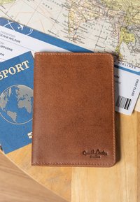 Porta passaporto in pelle marrone su un tavolo di legno, accanto a un passaporto blu, una carta d'imbarco e una mappa del mondo vintage.