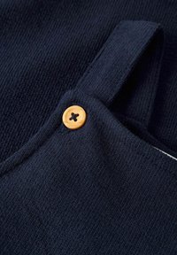 Marinblått texturerat tyg med en framträdande tan-knapp som stänger ett spänne, med ribbat mönster och mjuk, andningsbar textur.