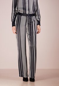 Black and white striped high-waisted trousers with a loose fit, made from smooth fabric. Features a flat waistband and wide leg design.