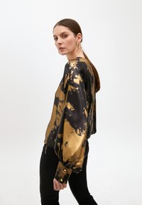 Blusa a maniche lunghe in nero e oro con una stampa tie-dye, realizzata in tessuto liscio, caratterizzata da una vestibilità morbida e polsini con bottoni.