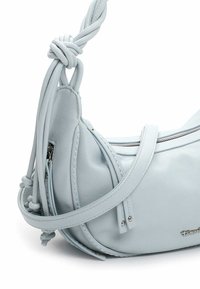 Hele sinine nahast käsitasku kõveras vormis. Omab sõlmede detailidega rihma, tõmblukuga sulgemist ja peeneid õmbluse aktsente.