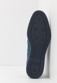 Baskets en mesh bleu avec une semelle en caoutchouc texturée présentant un motif hexagonal et un marquage subtil, conçues pour le confort et la respirabilité.