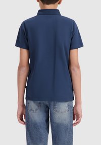 Navyblauwe korte mouwen polo met een kraag, gemaakt van katoen; gedragen met lichtblauwe denim jeans met een vervaagde was en achterzakken.
