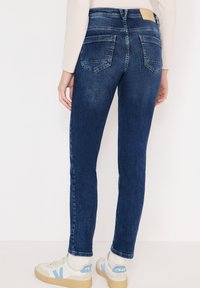 Tmavě modré úzké džíny s mid-rise pasem, zadními kapsami a lehkým vyblednutím. Kombinovány s bílými teniskami.