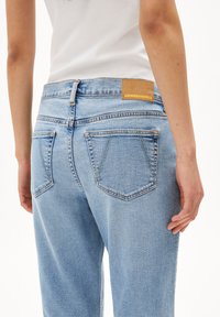 Jeans en denim bleu clair avec une coupe droite, présentant une étiquette en cuir portant le nom "ARMEDANGELS" au niveau de la taille et deux poches arrière.