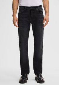 Jeans in denim nero con un taglio dritto, dotati di cinque tasche, chiusura con bottone e sfumature leggere per texture e stile. Abbinati a scarpe nere.