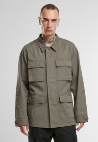 Chaqueta ligera verde oliva con cuatro bolsillos frontales, cierre de botones y cuello. Fabricada con un tejido duradero y con un corte relajado.
