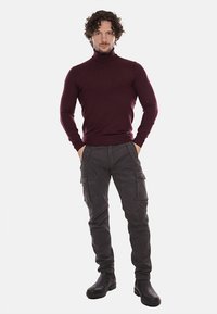 Maglione a collo alto color bordeaux abbinato a pantaloni cargo grigi. L'outfit presenta un design aderente e un tessuto testurizzato, completato da stivali neri.