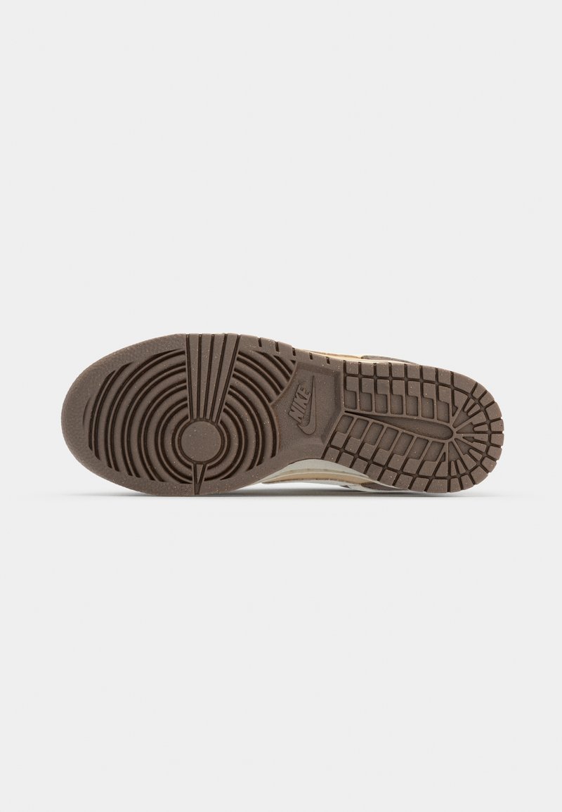 Semelle de basket Nike avec un motif en caoutchouc brun texturé, présentant des designs circulaires et linéaires, ainsi qu'un logo visible sur le côté.