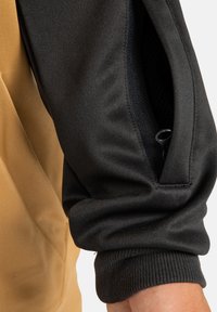 Czarna sportowa kurtka z teksturowanym wykończeniem i ściągaczami przy rękawach, z siateczkową wstawką i kieszenią na zamek.