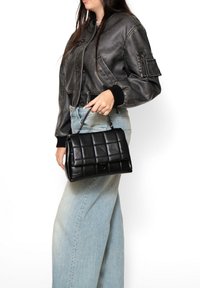 Borsa a tracolla nera in pelle trapuntata con una forma strutturata e chiusura a soffietto. Presenta un manico corto e una texture liscia.
