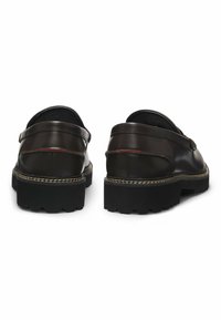 Bruine leren schoenen met een afgeronde vorm, met een dikke zwarte rubberen zool en decoratieve stiksels langs de rand.