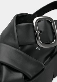 Black sandal with a wide, ruched leather strap and an adjustable metallic buckle. Notable for its chunky platform sole and smooth texture.