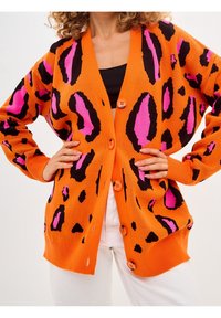 Orange cardigan with leopard print in black and pink. Features a button closure and ribbed cuffs, showing a loose fit and knit texture.
