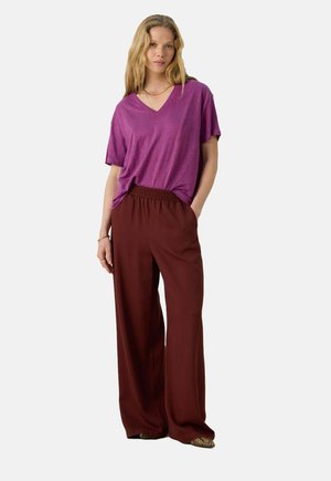 Purple v-neck t-shirt paired with wide-leg burgundy trousers featuring an elastic waistband. Smooth fabric with a relaxed fit.