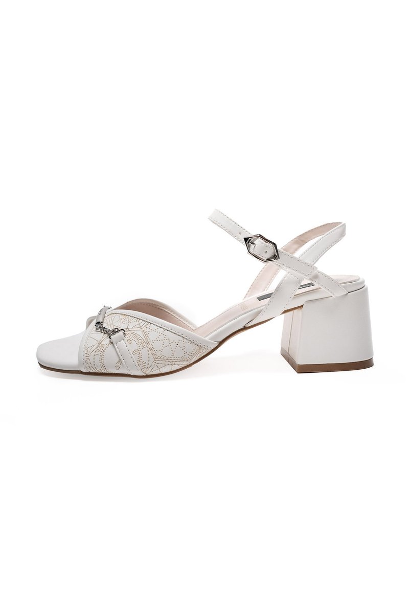 White heeled sandals, featuring an open toe, decorative strap detailing, block heel, and a textured patterned side panel. Adjustable ankle strap.