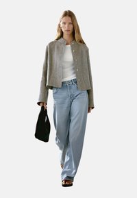 Szara lniana kurtka o kroju cropped, biała bluzka na ramiączkach, jasnoniebieskie dżinsy typu wide-leg oraz czarna torebka typu tote, noszone z czarnymi sandałami.