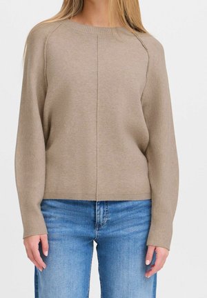 Maglione beige lavorato a maglia con maniche raglan, colletto a girocollo e dettagli di cucitura sottili. Abbinato a jeans in denim azzurro chiaro.