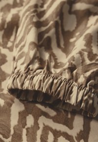 Tessuto marrone a fantasia con una texture che ricorda la stampa animale. Presenta un elastico arricciato sul bordo, che enfatizza morbidezza e flessibilità.