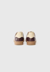 Baskets en cuir avec un schéma de couleurs bordeaux et crème, présentant une semelle en caoutchouc texturée, une forme arrondie et des embellissements de design minimalistes.