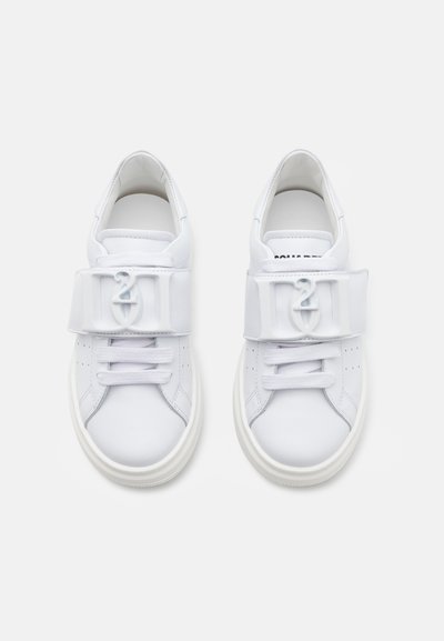 Vita sneakers med en slät läderstruktur, med en spänne över snörningen och en vit gummisula. Perforerade detaljer på sidorna.
