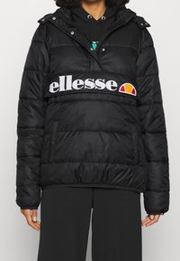 Chaqueta de plumas negra con capucha, que presenta una prominente banda de logotipo blanca en el pecho. Diseño texturizado y acolchado con bolsillos laterales.