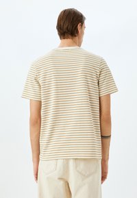 Camiseta de manga corta a rayas en color crema con rayas horizontales marrones. Tela suave, cuello redondo, corte relajado, costuras visibles y dobladillo recto.