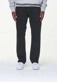 Svarta jeans av denim med rak passform, med minimal sömnad och två sidofickor. Matchat med vita sneakers mot en neutral bakgrund.