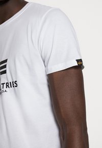 Weißes Baumwoll-T-Shirt mit einem schwarzen Grafikdruck auf der Brust und einem kleinen Etikett am Ärmelsaum. Klassisches Rundhalsausschnitt-Design.