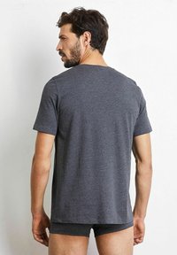 Grå t-shirt med kort ärm i mjuk bomullsblandning, med rund krage. Synlig sömnad längs sömmarna, tillsammans med mörka shorts.