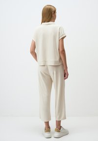 Beiges Loungewear-Set besteht aus einem kurzärmeligen Oberteil mit Kragen und lockeren Hosen, gefertigt aus weichem Stoff. Die Sneakers sind weiß mit einem beigen Akzent.