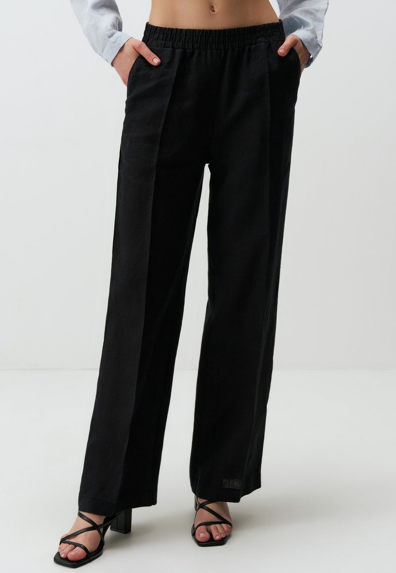 Zwarte wijde broek met een elastische tailleband, een soepele textuur, plooien aan de voorkant en zakken, gecombineerd met zwarte sandaaltjes met banden.